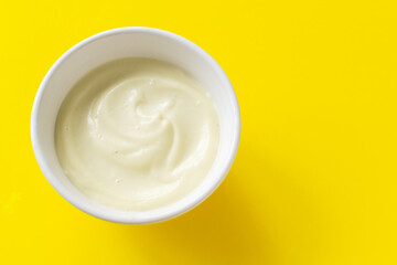 Homemade mayonnaise in a white bowl on a yellow background. The concept of proper nutrition. Creative. Minimalism. Horizontal orientation. Copy space.