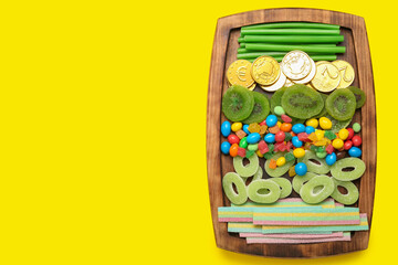 Wooden board with different sweets for St. Patrick's Day celebration on yellow background