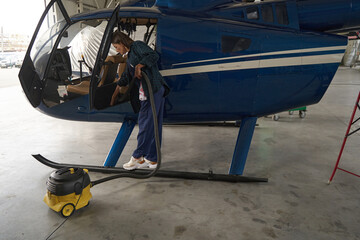 Young woman using vacuum cleaner while working in cockpit of airplane