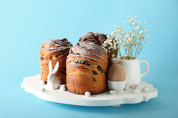 Wooden board with delicious Easter cake, gypsophila flowers and egg on blue background