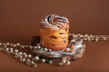 Wooden board with delicious Easter cake and pussy willow branches on brown background