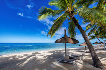 Palm trees and straw umbrellas and tropical sea in Mauritius island. Summer vacation and tropical beach concept.