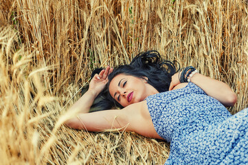 Happy young dreamy woman lying in a wheat field
