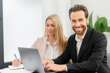 Obraz premium Young attractive man and woman working with papers and laptop in modern office. Blonde girl making notes on paper documents while working with a laptop