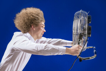 A man with curly hair holds a fan in his hands. The fan blows the guy away. Hair develops in the...