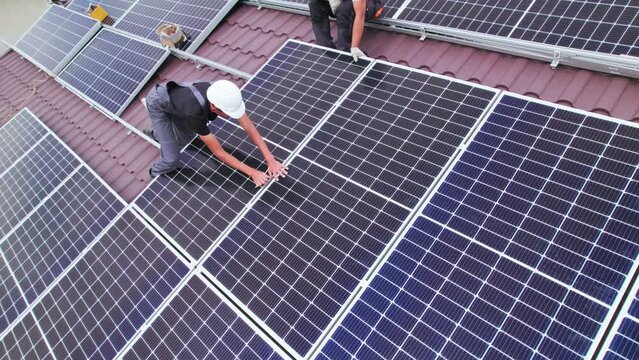 Men workers installing photovoltaic solar moduls on roof of house. Engineers in helmet building solar panel system outdoors. Concept of alternative and renewable energy. Aerial view.