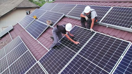Men workers installing photovoltaic solar moduls on roof of house. Engineers in helmet building solar panel system outdoors. Concept of alternative and renewable energy. Aerial view. - Powered by Adobe