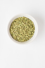 Top view of green aromatic fennel seeds in the ceramic bowl on white background. Fennel is ingredient of traditional Indian cuisine Ayurvedic nutrition