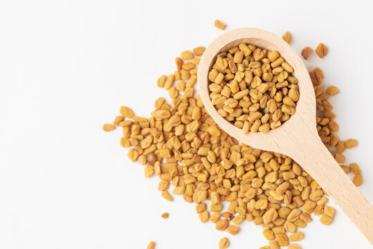 Macro photo of dry yellow fenugreek seeds or shambhala, helba seeds in wooden spoon on white background, top view