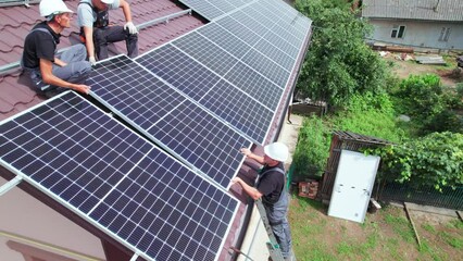 Men workers installing photovoltaic solar moduls on roof of house. Engineers in helmet building solar panel system outdoors. Concept of alternative and renewable energy. Aerial view.