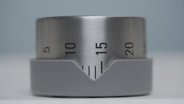 Silver kitchen timer with numbers rotates and counts timelapse. Egg timer, kitchen alarm clock, countdown minutes. Clockwork for time lapse during cooking, close up on a gray background. Slow motion.