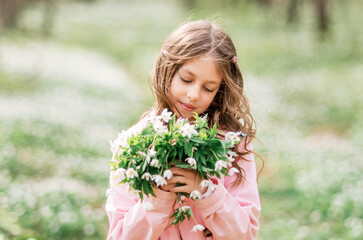 Close-up portrait of a girl with primroses. A child in the spring forest admires a bouquet.