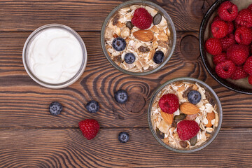 Homemade granola with nuts, raspberries and blueberries, yogurt on a wooden rustic table, top view, copy space. healthy breakfast