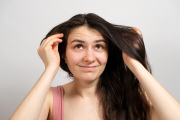 Naklejka premium A beautiful brunette woman with long hair on a white background holds her hands on her head and thinks about what hairstyle to do