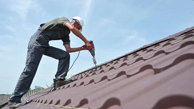 Worker prepearing to installation photovoltaic solar panel system on the roof of house. Close up man installer working with electric screwdriver on blue sky background.