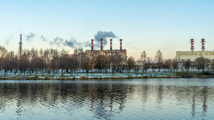 Fototapeta premium Smoking chimneys of a thermal power plant against a winter cloudy sky. Ecological problems concept. Space for text.