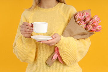 Young woman with bouquet and coffee on yellow background