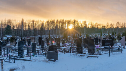 Winter sunset over a snow covered cemetery with dark headstones and trees. Afterlife. Samsara concepts.