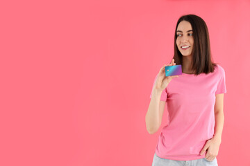 Attractive woman in t-shirt holds card on pink background