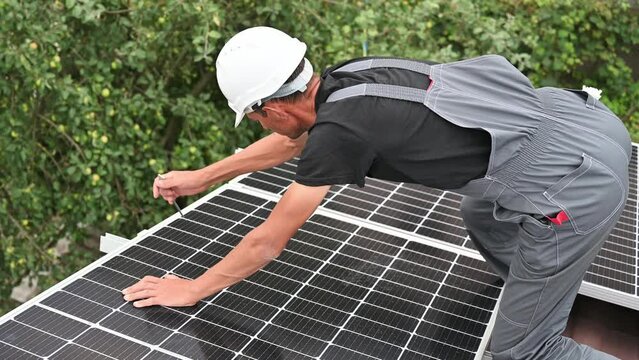 Man worker mounting photovoltaic solar moduls on roof of house. Close up of electrician installing solar panel system outdoors, tightening with hex key. Concept of alternative and renewable energy.