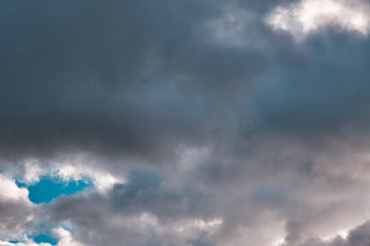 Dark dense cumulus clouds, deep textured & dramatic with a small tiny glimpse of blue sky.