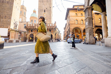 Stylish woman walks the street on background of famous towers in Bologna city. Italian lifestyle...