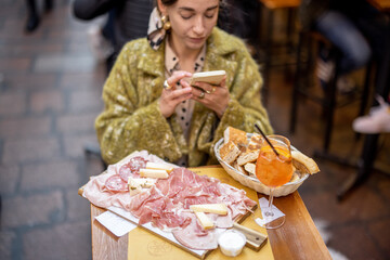 Woman photographing plate with Italian meat appetizer and Spritz Aperol drink while sitting at...