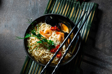 Asian soup with noodles ramen, with miso paste, soy sauce, mussels and shrimps prawn. On a dark stone table, with chopsticks. Copy space