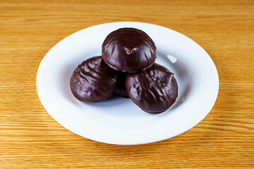 Stacked chocolate marshmallow  3 pieces, on a white plate in the center of the table. Angle view of chocolate covered cookie in the center of a white round plate 