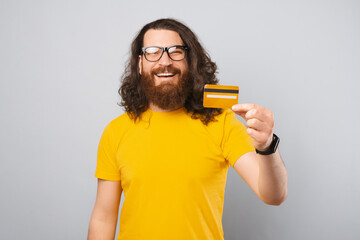 Happy young man with beard and long hair showing yellow blank credit card.