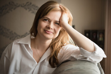 Happy smiling peaceful blond hair woman sitting on a couch at home and support her head with hand. relaxing on sofa at home