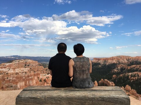 Rear View Of Couple Sitting On Rock Against Sky
