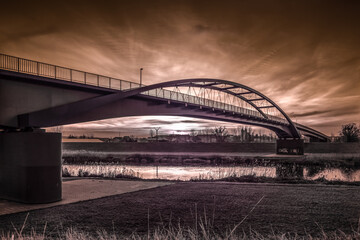 Fototapeta ogromny most nad rzeką i dramatyczne wieczorne niebo z zachodzącym słońcem obraz