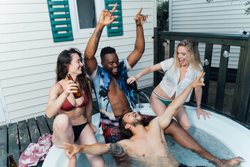 Four multiracial friends enjoying, laughing and drinking in a jacuzzi in summertime