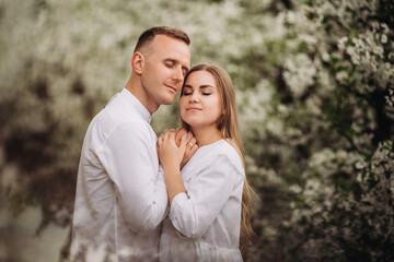 Young loving couple in a walk in a spring blooming apple orchard. Happy married couple enjoy each...