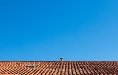 Against backdrop of clear blue sky, a contrasting orange roof made of old tiles