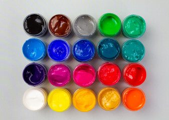 Open jars with gouache of different colors close-up on a gray background. Hobby - painting
