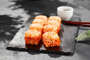 Baked Maki sushi on dark slate. Hot california maki with tobiko. Sushi roll with masago caviar, cheese topped baked oven. Style concept japanese menu with black background, leaves and hard shadow.