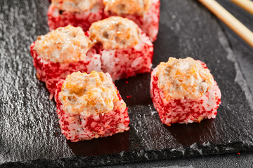 Baked Maki sushi on dark slate. Hot sushi roll with salmon. Sushi roll with tobiko outside, baked fish  and cheese topped. Style concept japanese menu with black background, leaves and hard shadow.