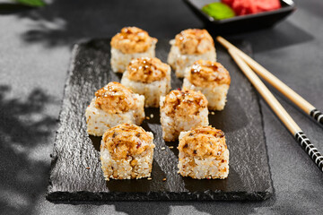 Baked Maki sushi on dark slate. Hot unagi maki with eel. Sushi roll with baked eel, cheese and unagi sauce topped. Style concept japanese menu with black background, leaves and hard shadow.