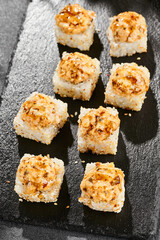 Baked Maki sushi on dark slate. Hot unagi maki with eel. Sushi roll with baked eel, cheese and unagi sauce topped. Style concept japanese menu with black background, leaves and hard shadow.