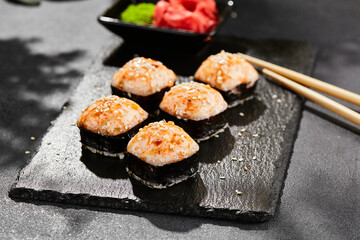 Baked Maki sushi on dark slate. Hot unagi maki with tobiko. Sushi roll with baked cheese, masago and unagi sauce topped. Style concept japanese menu with black background, leaves and hard shadow.