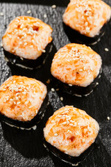 Baked Maki sushi on dark slate. Hot unagi maki with tobiko. Sushi roll with baked cheese, masago and unagi sauce topped. Style concept japanese menu with black background, leaves and hard shadow.