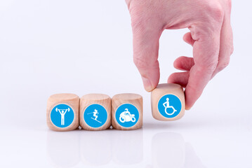 Eine Hand legt verschiedene Symbole mit sportlichen Aktivitäten wie Gewichtheben, Skifahren oder Motorradfahren und das Symbol eines behinderten Rollstuhlfahrers