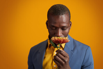 African-American young man in yellow shirt and blue jacket smelling flower while standing in front...