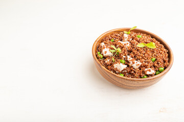 Fototapeta na wymiar Quinoa porridge with green pea and chicken in wooden bowl on a white wooden background. Side view, copy space.
