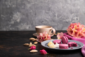 Purple macarons or macaroons cakes with cup of coffee on a black concrete background. Side view, selective focus, copy space.