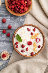 Rice flakes porridge with milk and strawberry in wooden bowl on gray wooden background. Top view, close up.