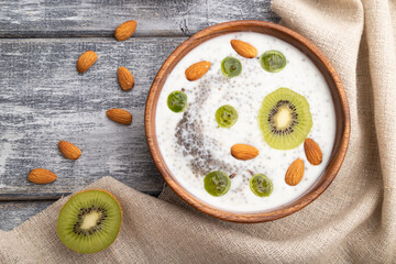 Yogurt with kiwi, gooseberry, chia and almonds in wooden bowl on gray wooden background. top view, flat lay.