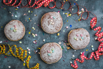 Krapfen, Berliner or donuts with streamers, confetti and mini marshmallows on blue background. Colorful carnival or birthday image, top view